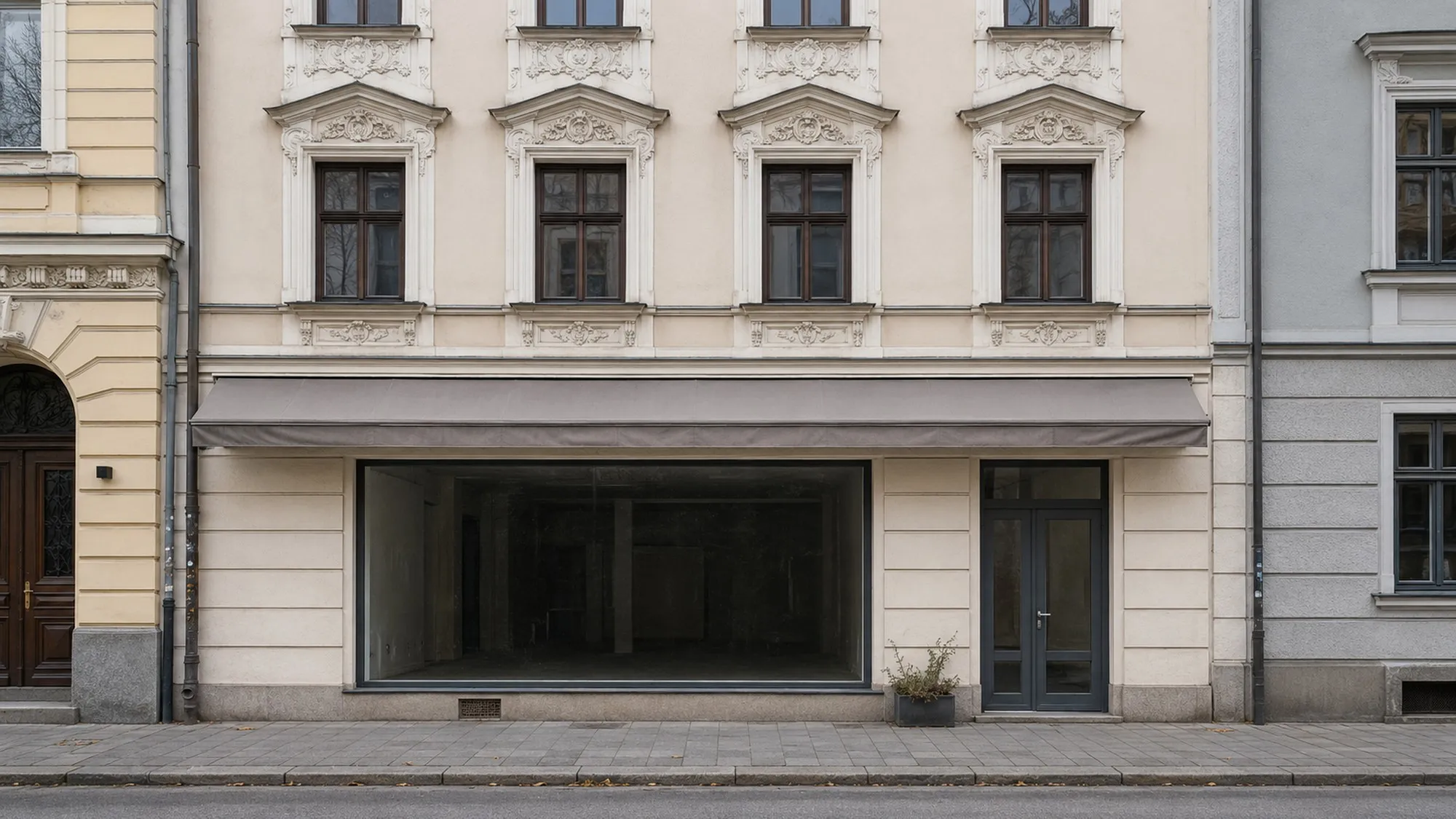 Leerstehende, gepflegte Ladenfront mit grauer Markise und leerem Schaufenster, stille Straße